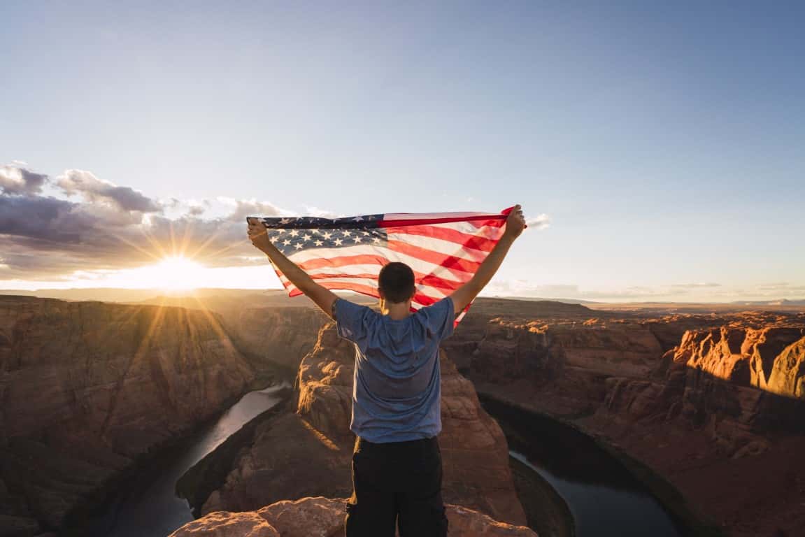 USA, Arizona, Colorado River, Horseshoe Bend, young man on viewpoint with American flag